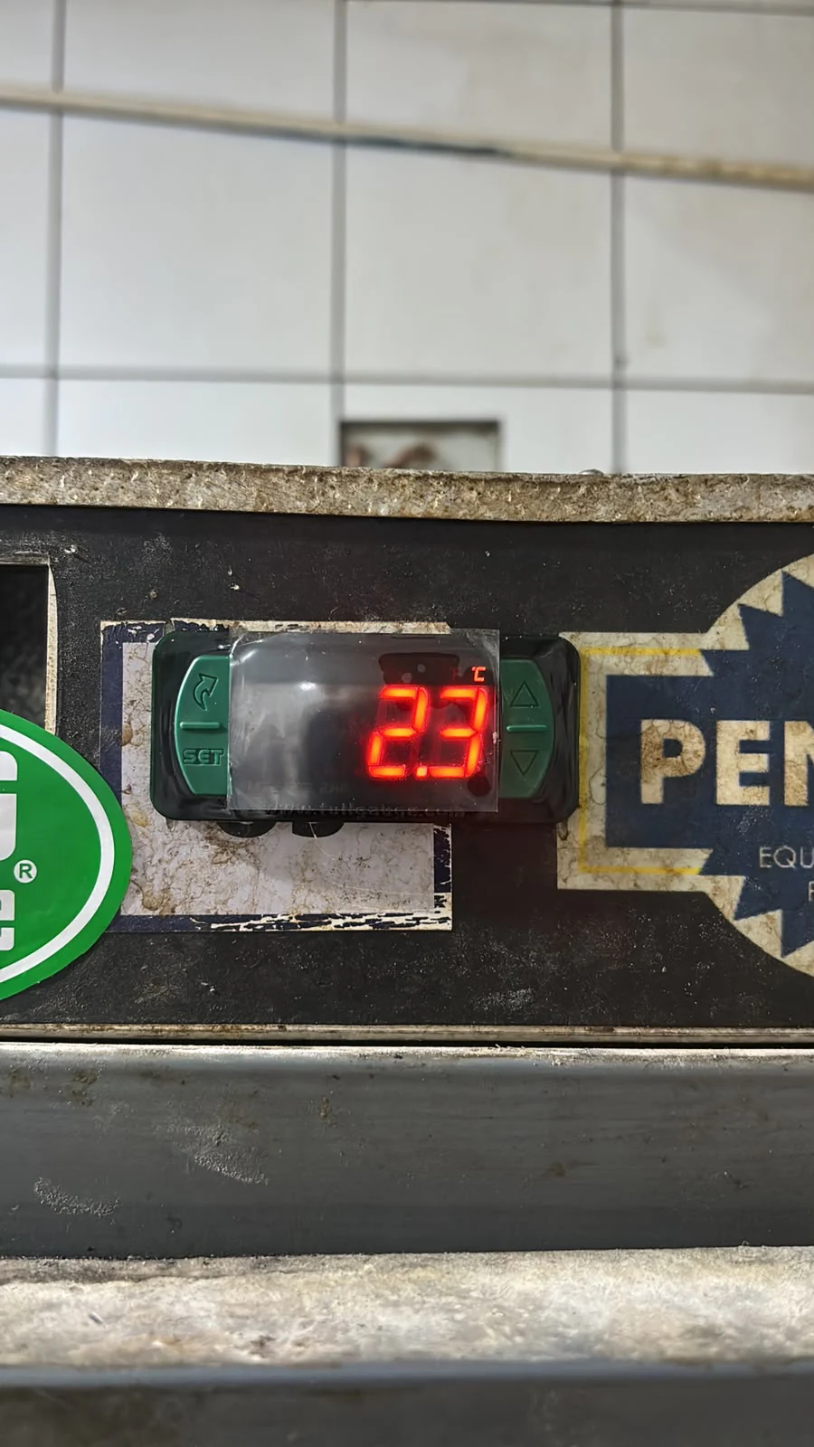 Controlador digital de temperatura de câmara fria, com display vermelho marcando 23°C, instalado no painel do equipamento.