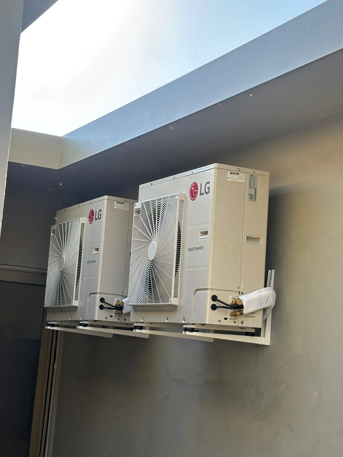 Duas condensadoras LG instaladas lado a lado em suporte de parede, em recuo de concreto claro com entrada de luz natural.